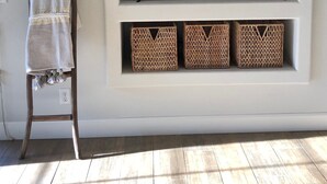 Een woonkamer met een aan een witte muur bevestigde televisie, een houten ladder en rieten manden op planken onder de televisie.