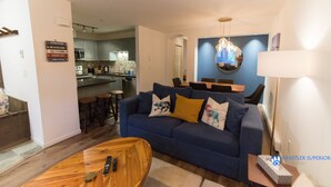 Un salon moderne avec un canapé bleu, une table basse en bois et une cuisine en arrière-plan.