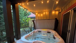 Un bain à remous doté d’un panneau de commande, entouré de guirlandes lumineuses et offrant une vue sur une maison et la verdure environnante.