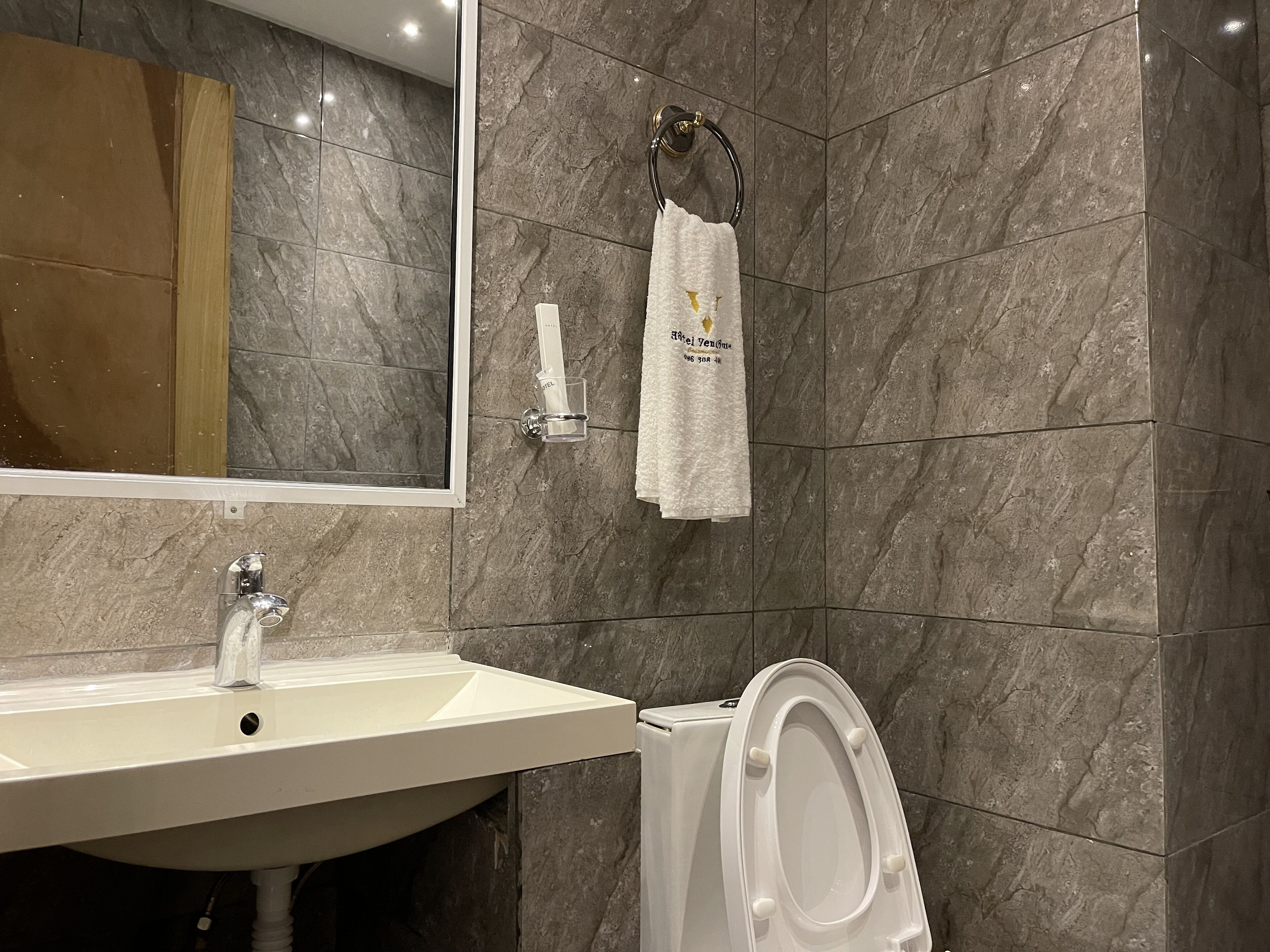 Un baño con lavamanos, espejo, toallero y retrete.