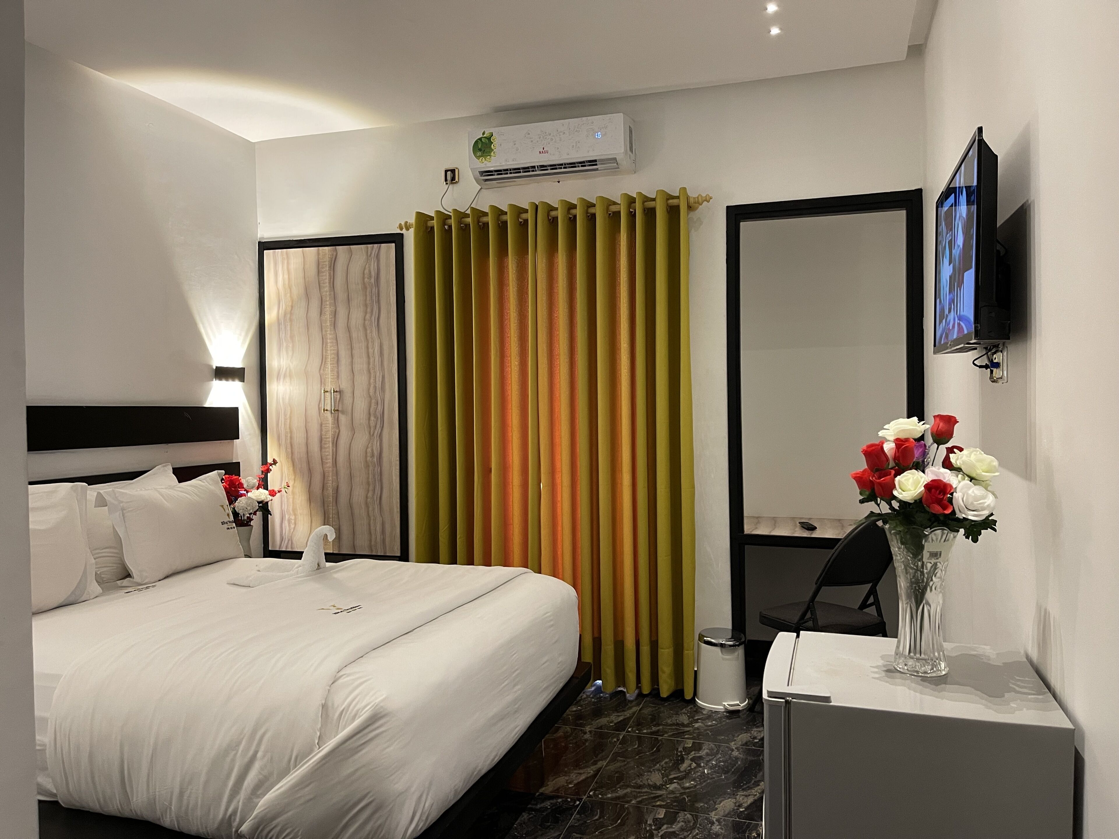 Ein Hotelzimmer mit Bett, Spiegel, Fernseher und einer Vase mit Blumen.