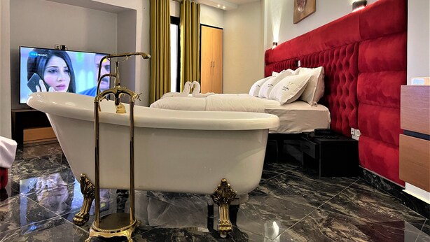 A modern bathroom with a freestanding bathtub, a vanity with a mirror, and a television displaying a program.