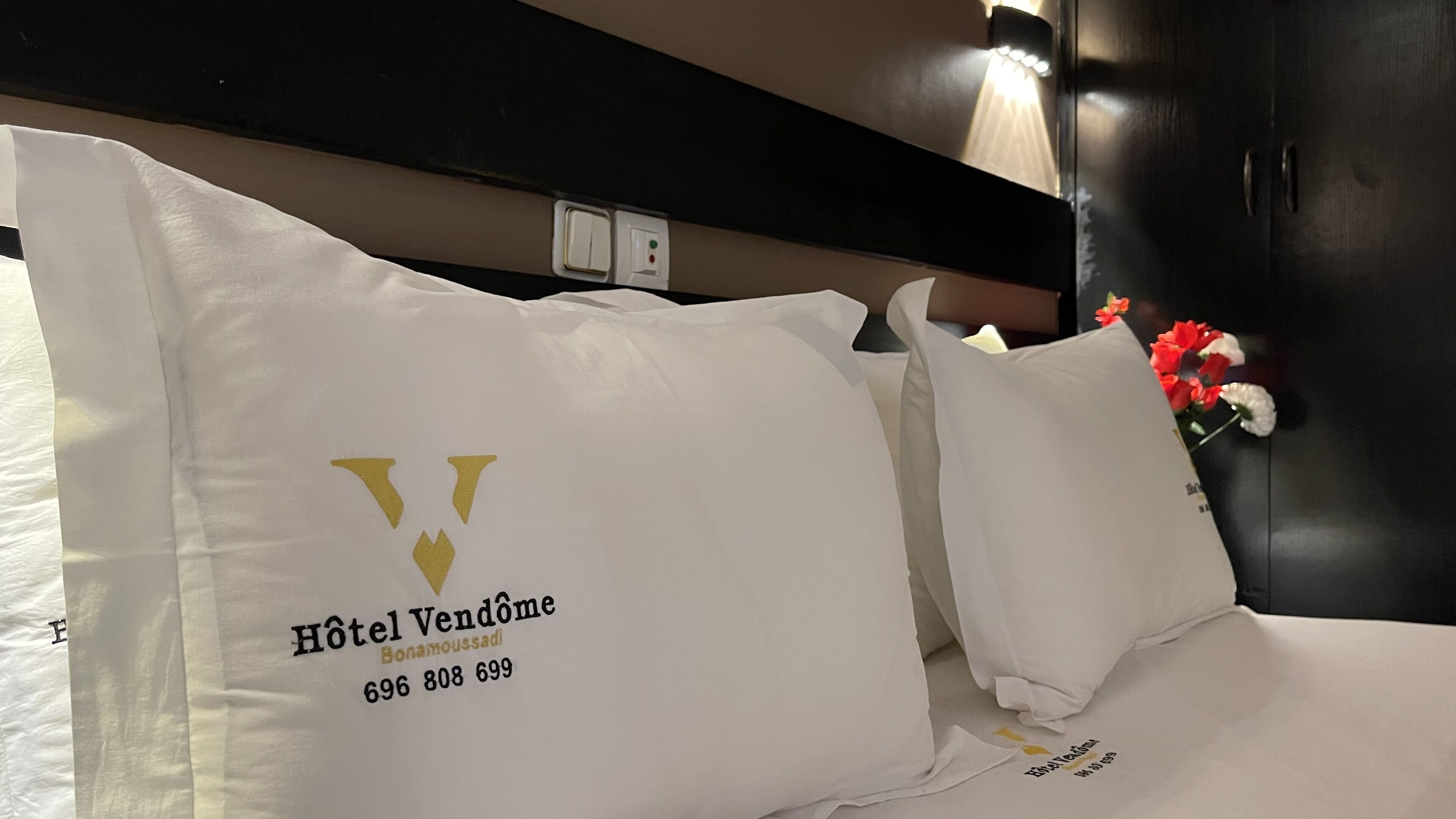 A hotel bed with a pillow featuring the Hotel Vendome logo and contact number.