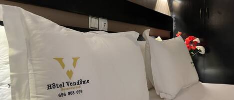 A hotel bed with a pillow featuring the Hotel Vendome logo and contact number.