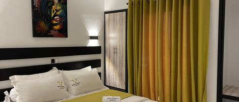 A hotel room with a bed, a painting on the wall, an air conditioning unit, and curtains.