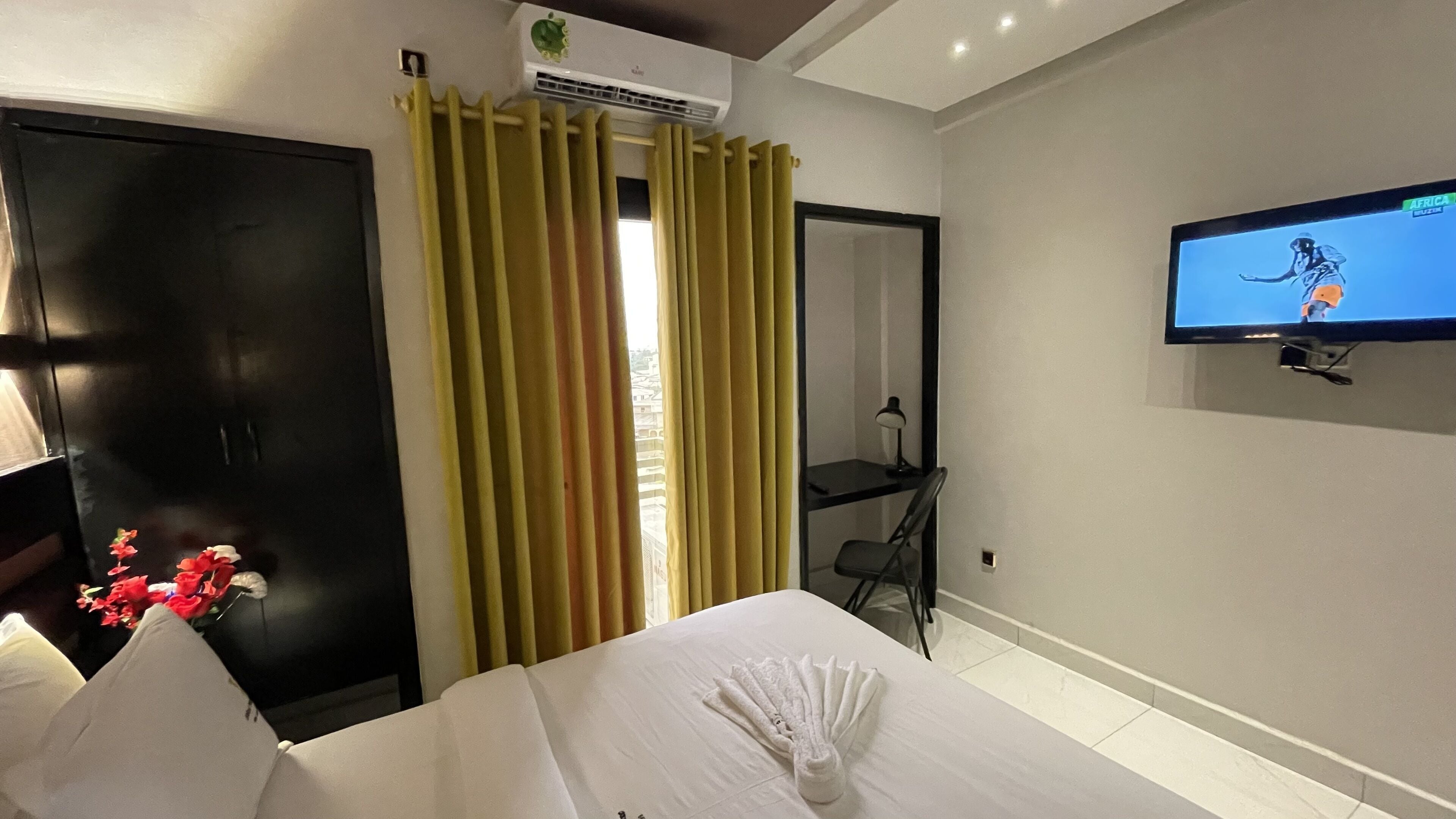 Una camera d'albergo con un letto, una scrivania, una televisione e una finestra con tende.