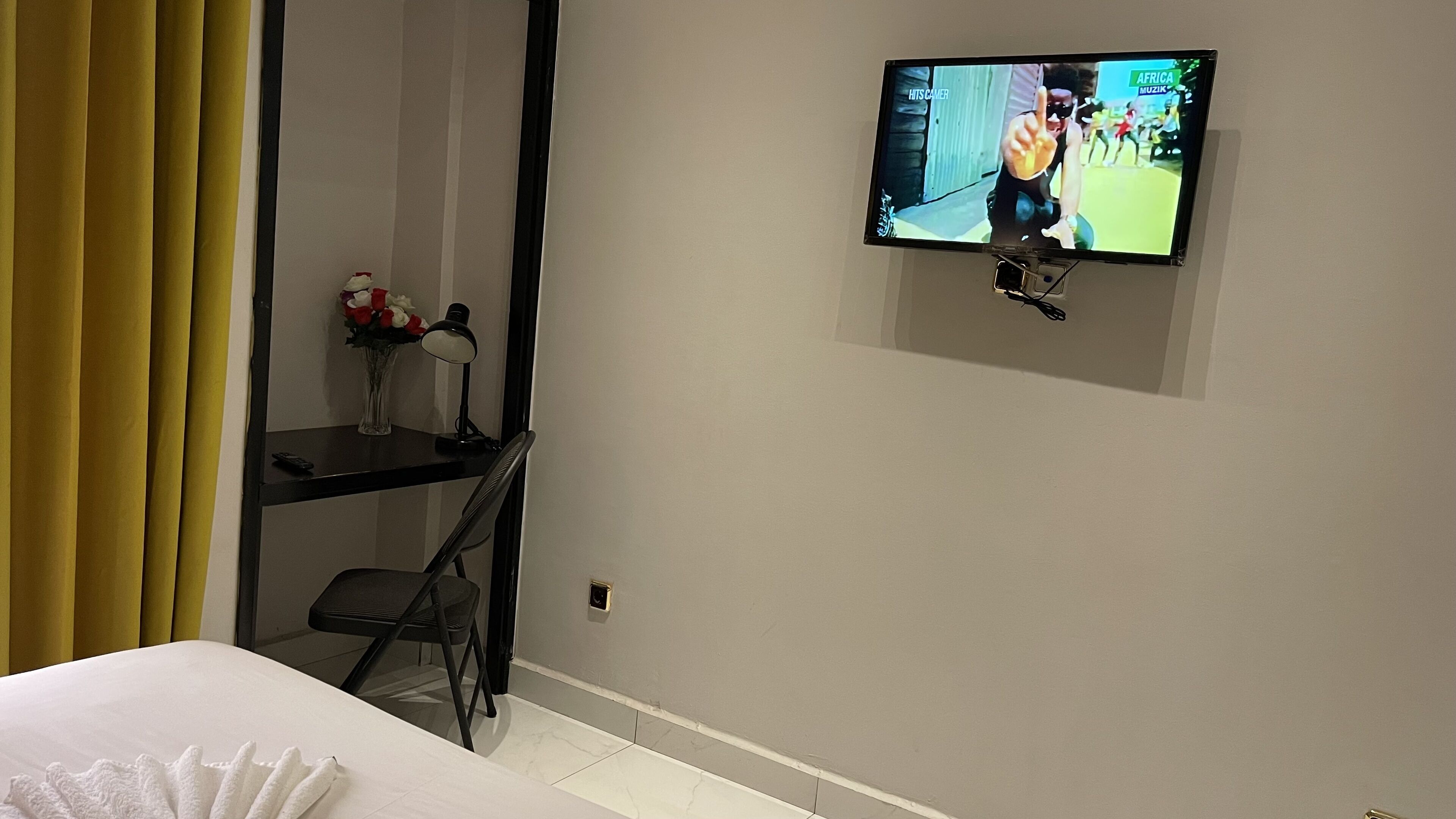 Habitació d'hotel amb llit, escriptori amb làmpada, cadira i televisió penjada a la paret que mostra un esdeveniment esportiu.