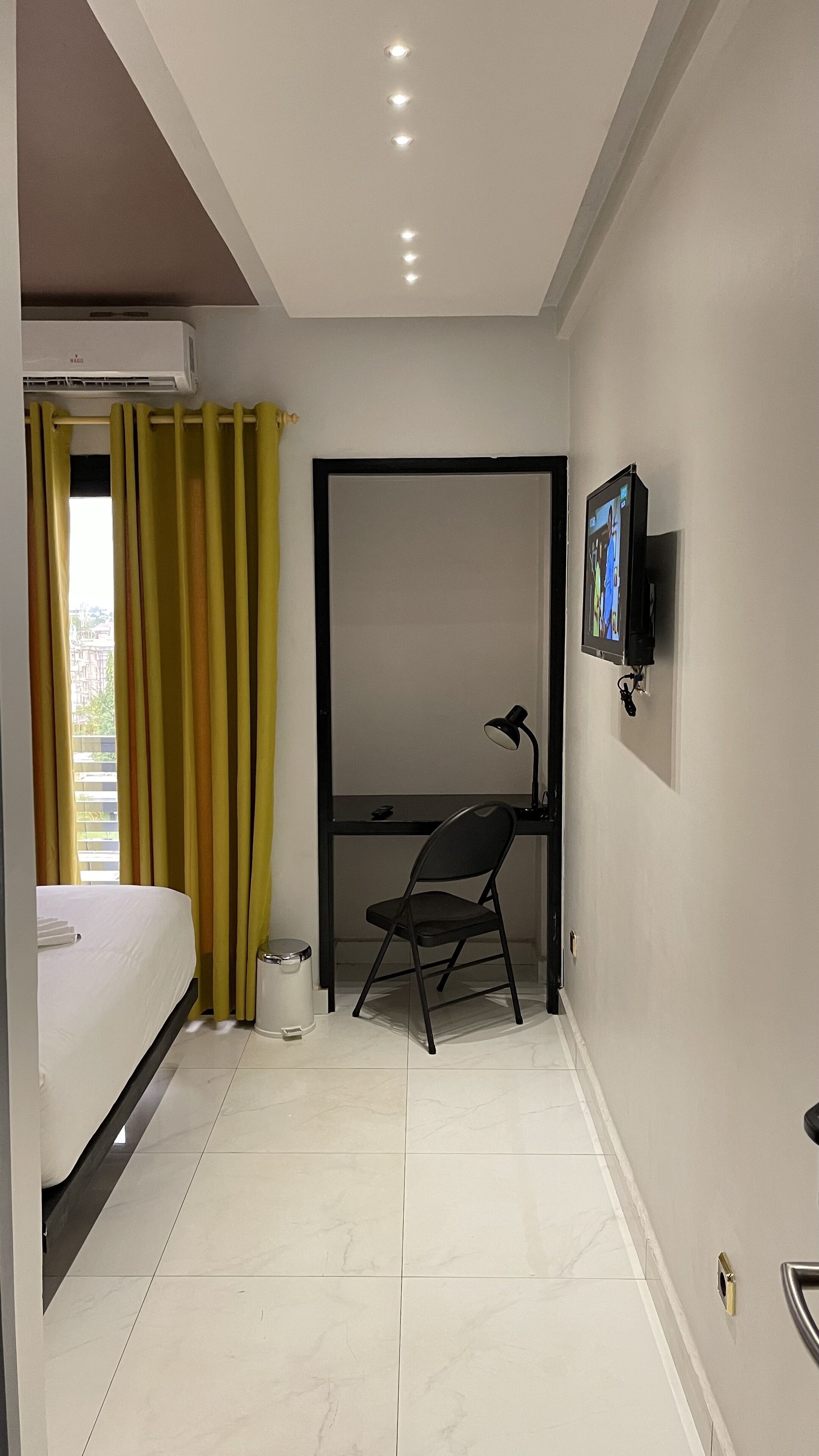 A bedroom with a bed, a desk, a chair, a TV, and a window with curtains.