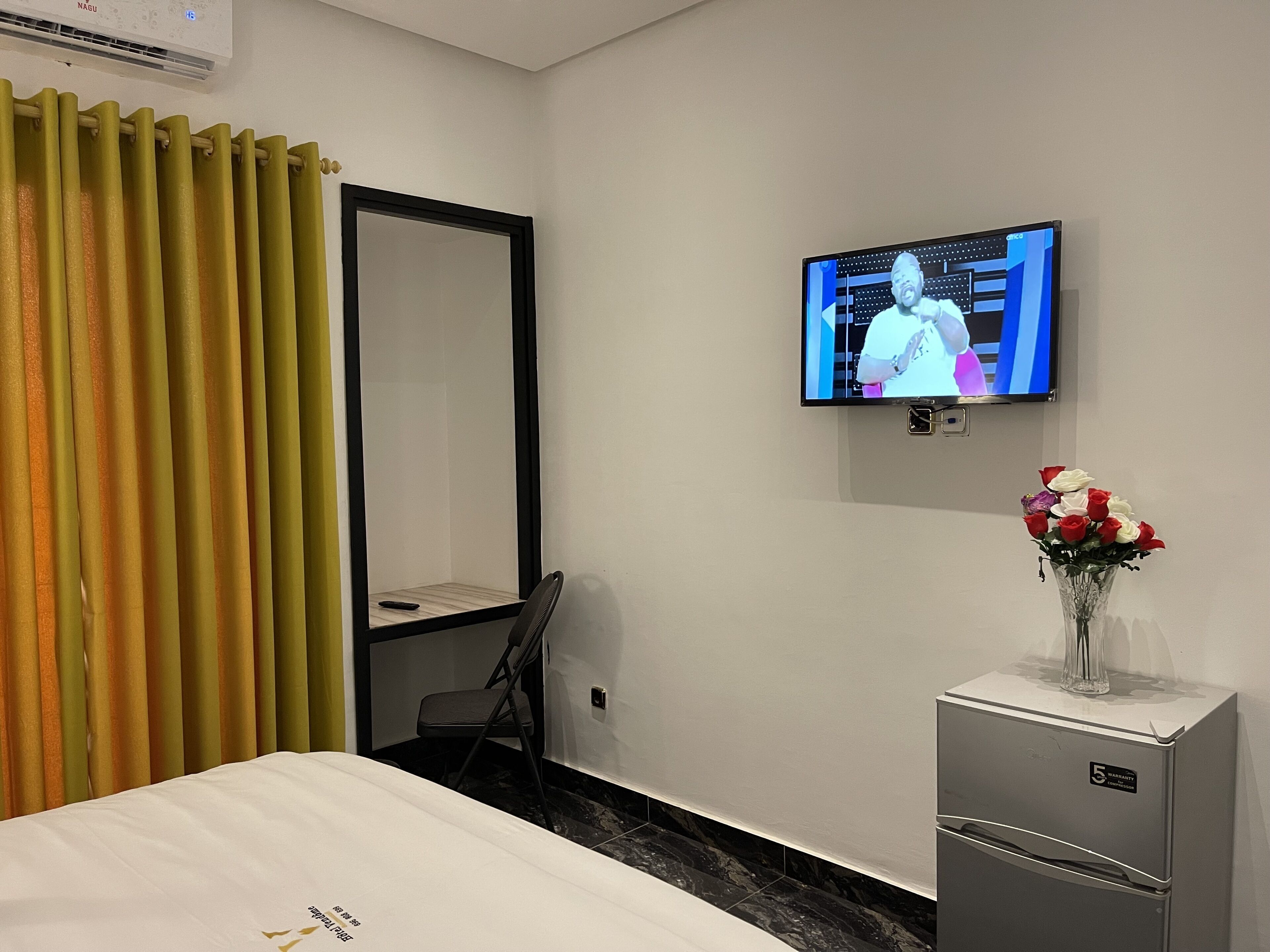Habitación de hotel con cama, televisor montado en la pared, un escritorio pequeño con silla y refrigerador.