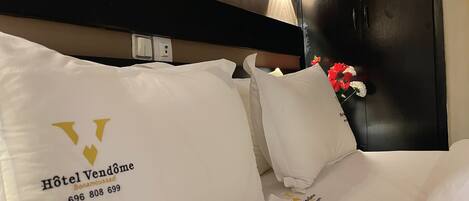 A hotel room with a bed, pillows, a nightstand, and a wall-mounted light.