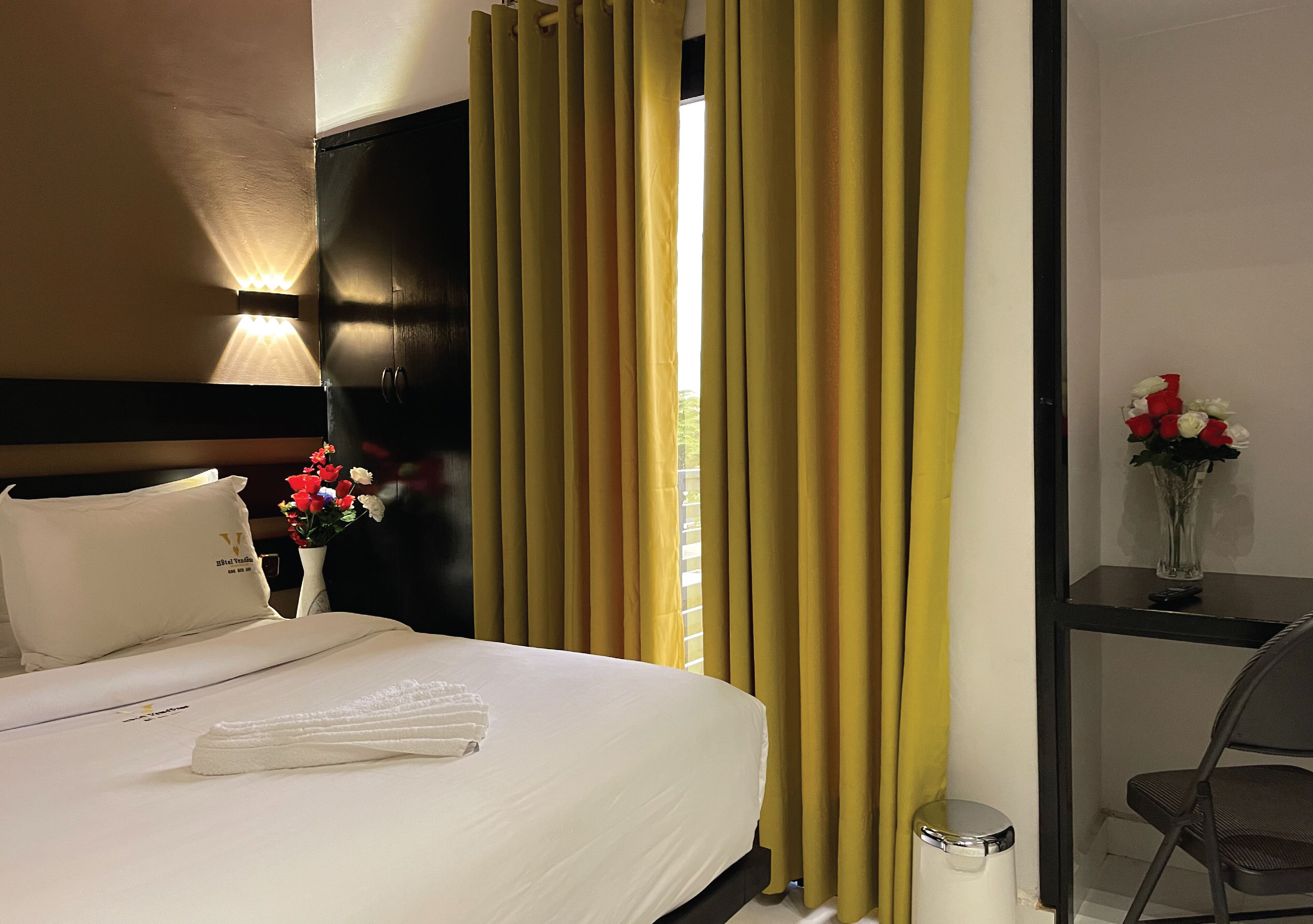 A hotel room with a neatly made bed, a bedside table with a vase of flowers, and a chair.