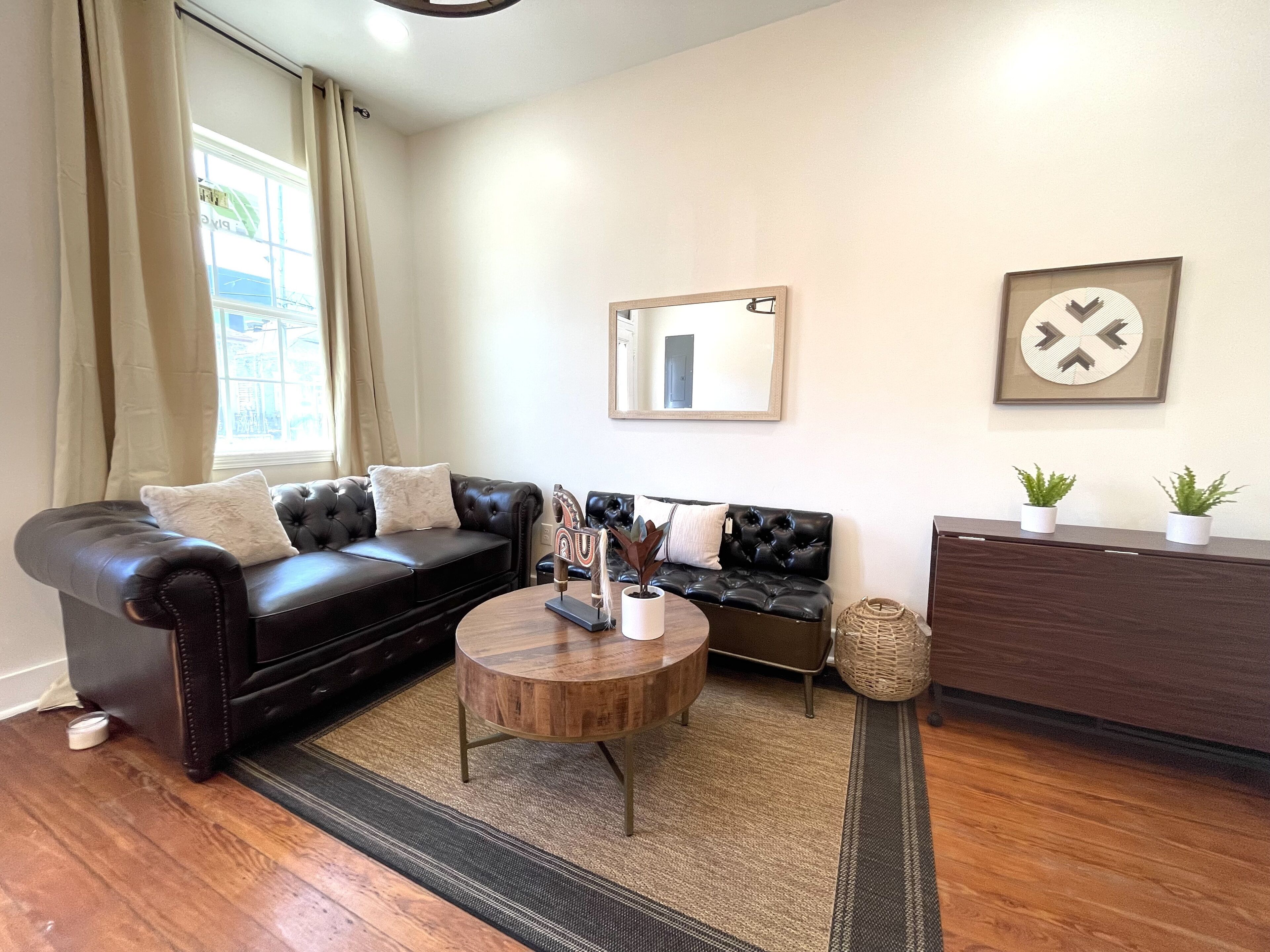 A living room with a black leather sofa, a round wooden coffee table, and a dark wooden cabinet.