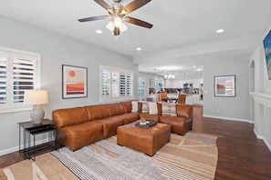 A spacious living room with a brown leather sectional sofa, a coffee table, and a ceiling fan.