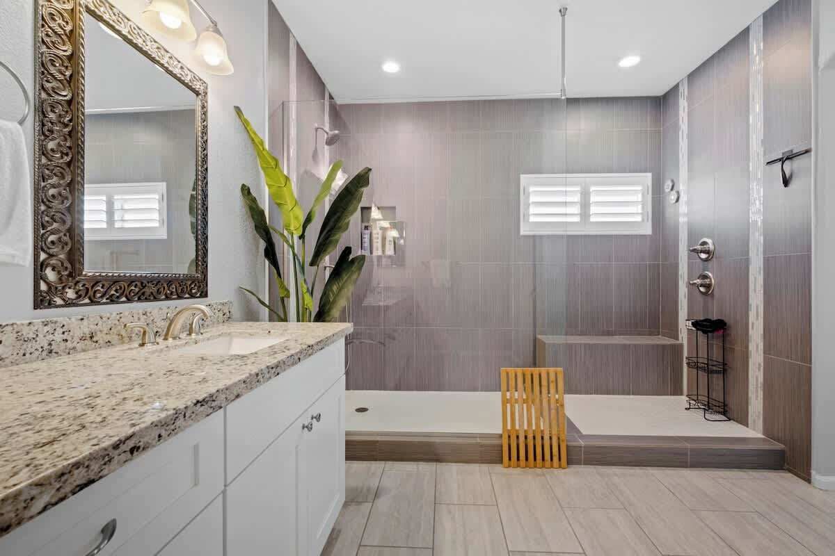 Ett modernt badrum med en bänkskiva i granit, en stor spegel och en duschhörna.
