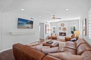 A living room with a brown leather sofa, a fireplace, and a ceiling fan.