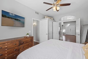 A bedroom with a bed, a ceiling fan, a dresser, and a painting of a beach.