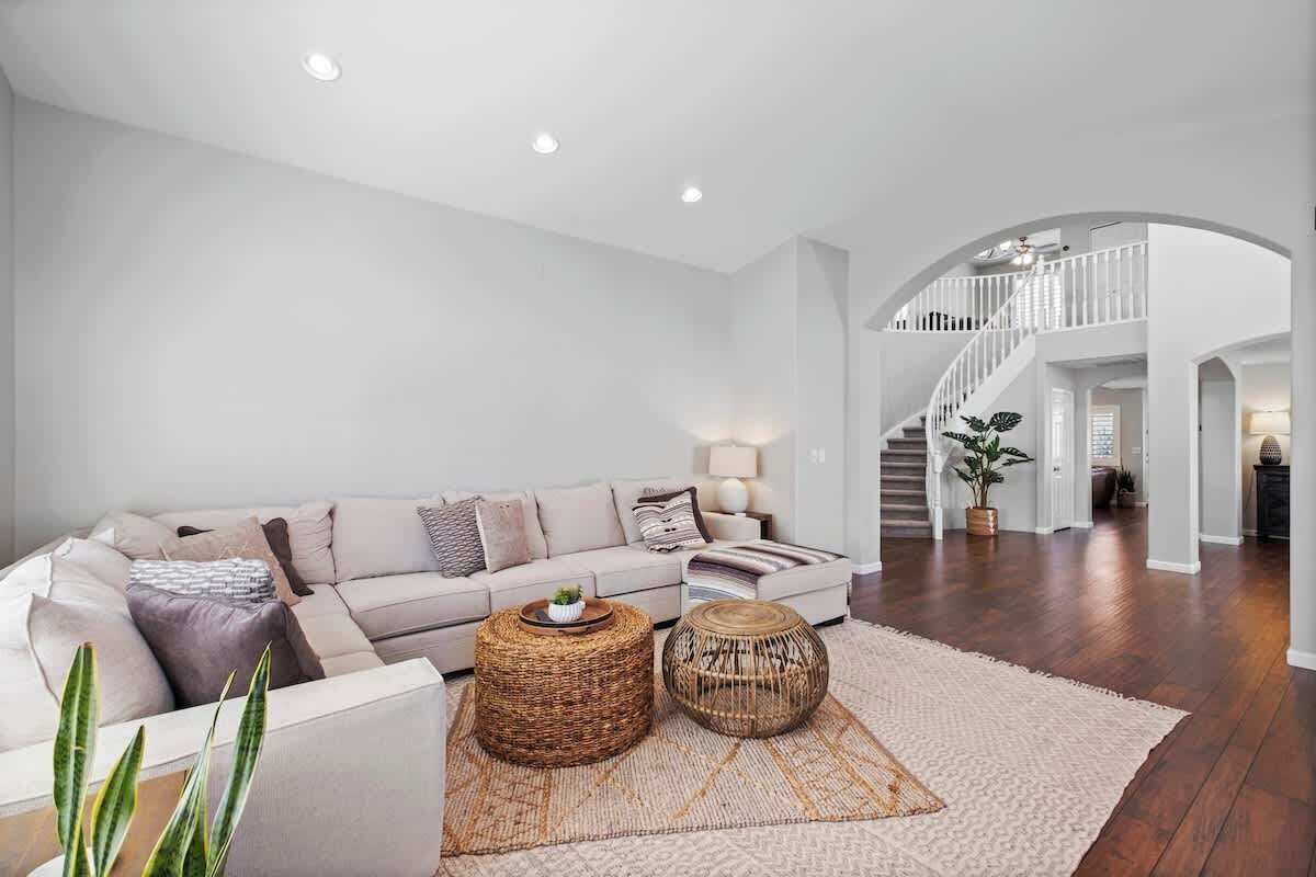 A spacious living room with a large sofa, two round wicker coffee tables, and a neutral rug. A staircase with a white railing leads to an upper level.