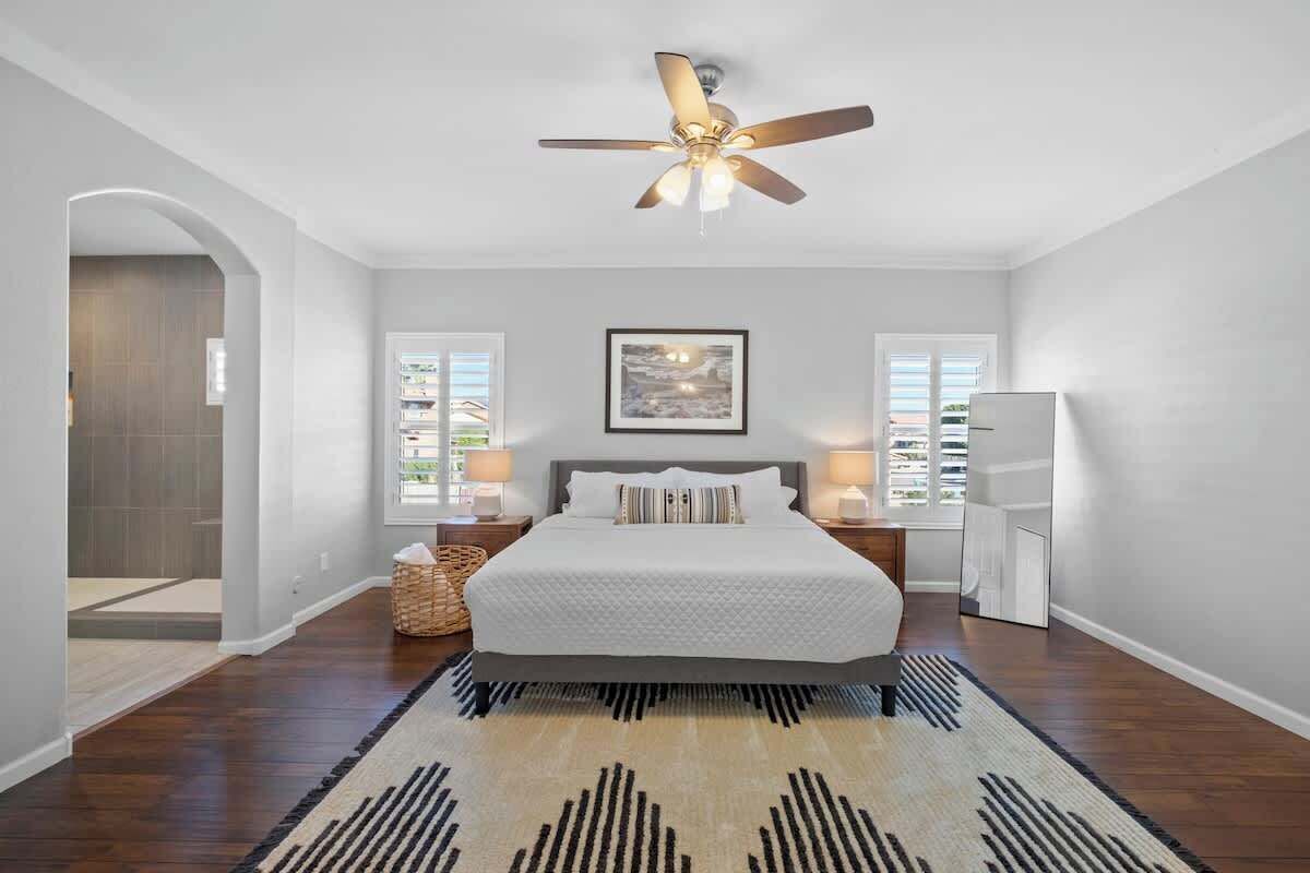 A bedroom with a bed, a ceiling fan, a rug, and a framed picture on the wall.