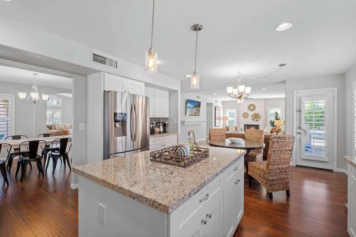 A spacious kitchen with granite countertops, stainless steel appliances, and a dining area with wicker chairs.