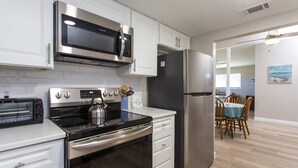 Une cuisine moderne avec des meubles blancs, un réfrigérateur en acier inoxydable, un four à micro-ondes, une cuisinière et un grille-pain.
