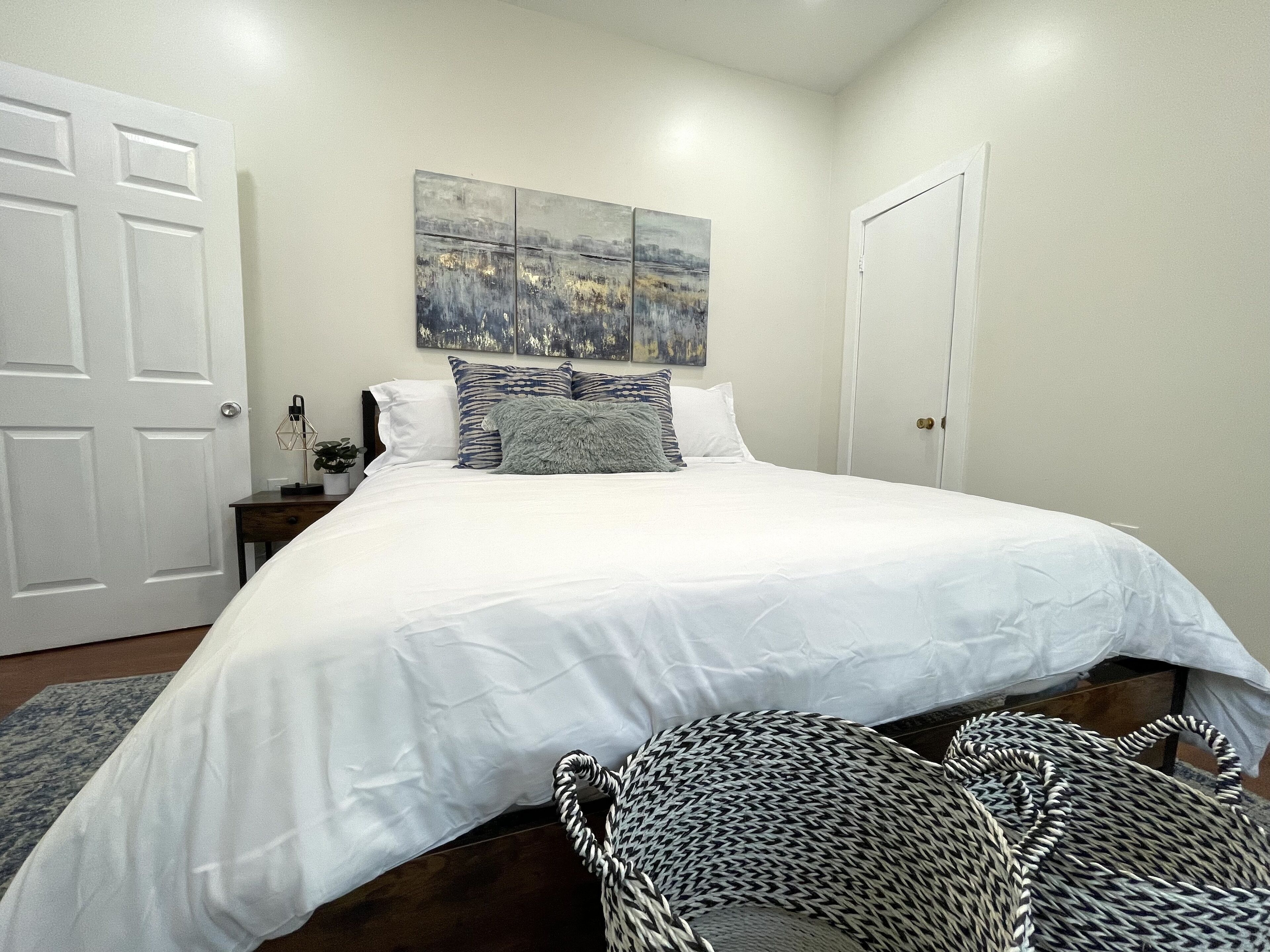 A bedroom with a large bed, a nightstand, a lamp, and a painting on the wall.