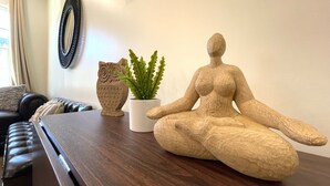 Una mesa de madera con una escultura de una figura meditando, una planta en maceta y un objeto con forma de lechuza.