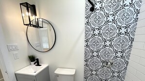 Un baño con inodoro blanco, lavamanos con espejo superior y bañera con azulejos estampados.
