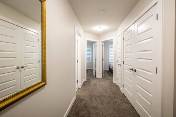A hallway with white doors, a large mirror, and carpeted flooring.