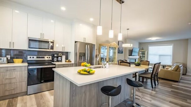Una cocina moderna con electrodomésticos de acero inoxidable, una isla central con taburetes y un comedor con sofá y sillas.