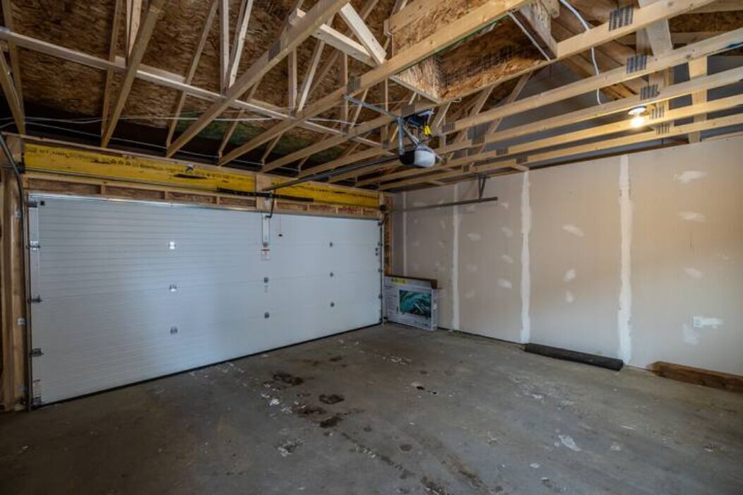 A garage with a closed white garage door, exposed wooden ceiling beams, and unfinished walls.