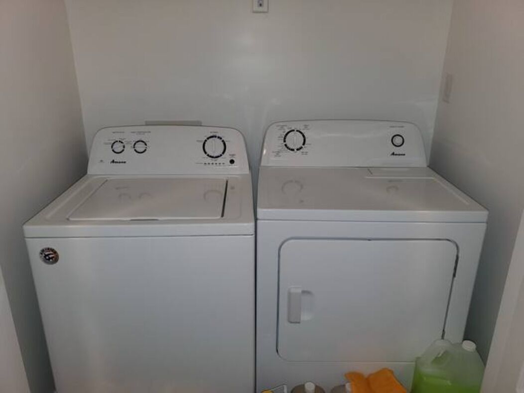Deux machines à laver à chargement frontal, de couleur blanche, se trouvent dans une buanderie, avec une seule prise électrique murale au-dessus.