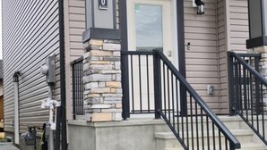 Un edificio residencial con detalles de piedra en el porche delantero, una escalera de metal negro y una puerta visible.