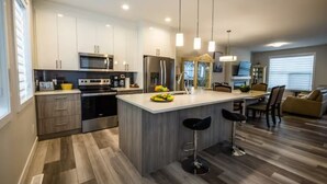 Una cocina moderna con gabinetes blancos, electrodomésticos de acero inoxidable y una isla central con taburetes de bar.