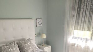 Un lit bien fait, avec une literie à motifs, une lampe de chevet et une fenêtre ornée de rideaux légers.