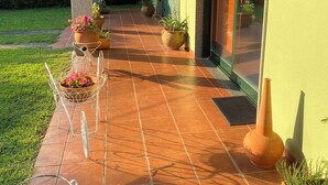 Une terrasse couverte, avec des carreaux de terre cuite, des plantes en pot et une jardinière suspendue.