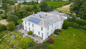 Un bâtiment blanc, doté d’un toit en pierre et de panneaux solaires, entouré de verdure et d’une pelouse bien entretenue.