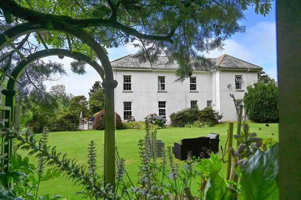 A white building with a symmetrical facade, a well-maintained lawn, and a garden with various plants.