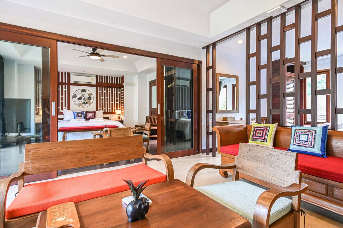 A hotel room with a wooden sofa set, a dining table with a vase, and a large mirror.