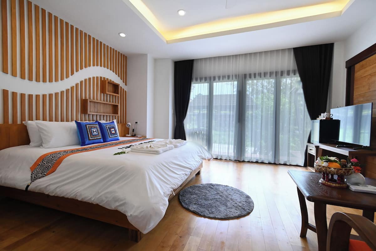 A modern hotel room with a large bed, wooden panel wall, a TV, and a dining area with a table and chairs.