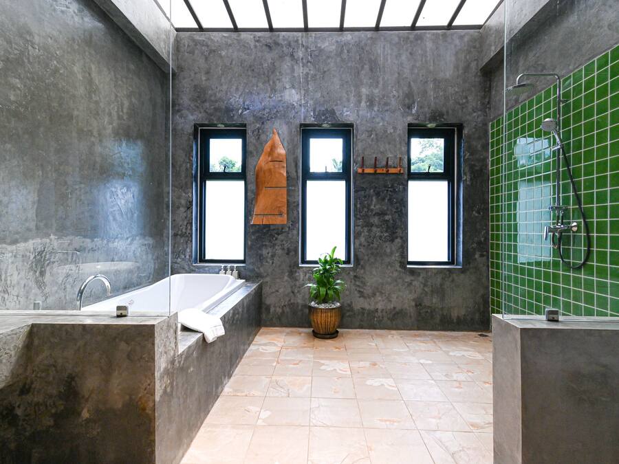 A modern bathroom with a large bathtub, two windows, a green tiled wall, and a potted plant.