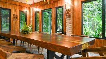 Un salón de conferencias con una larga mesa de madera y sillas, ventanas amplias que dan a zonas verdes y un adorno decorativo en la pared.