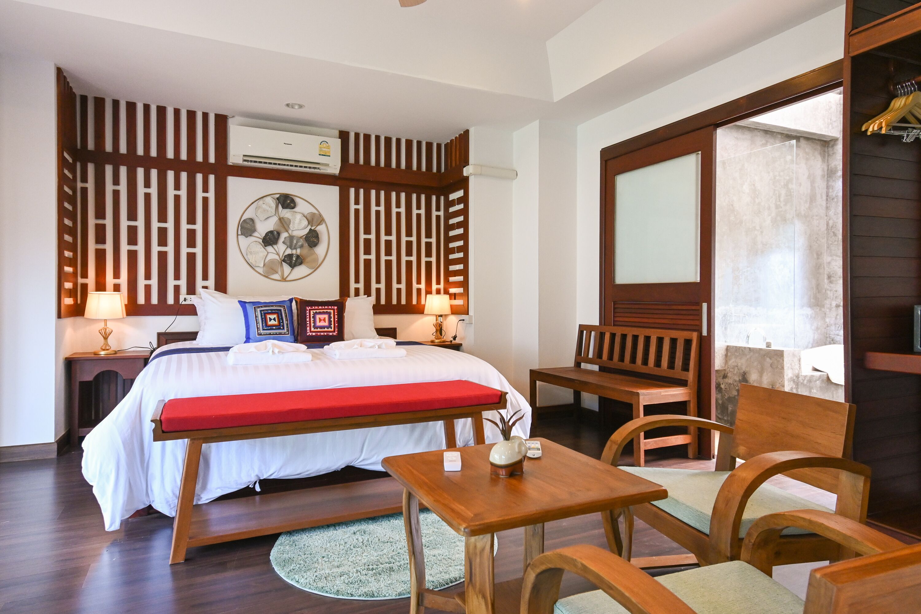 Habitación de hotel con cama, mesitas de noche, escritorio, sillas, alfombra redonda y un panel de madera con un adorno colgante.