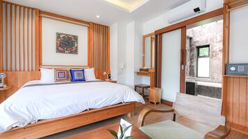 A modern hotel room with a large bed, wooden headboard, a small table, a bench, and a view of the outside.