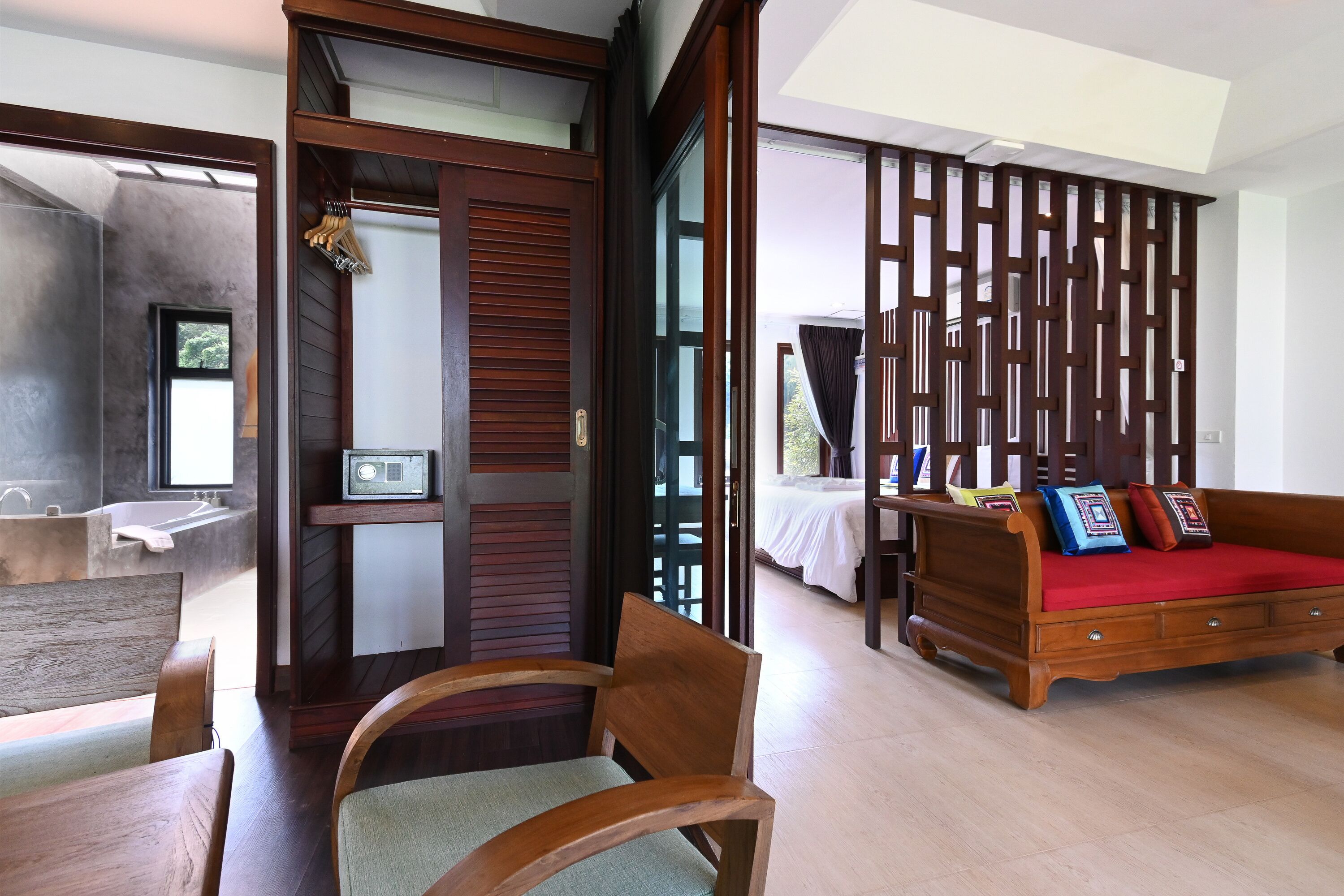 Une chambre d’hôtel moderne avec une chaise en bois, un canapé rouge et une grande fenêtre.