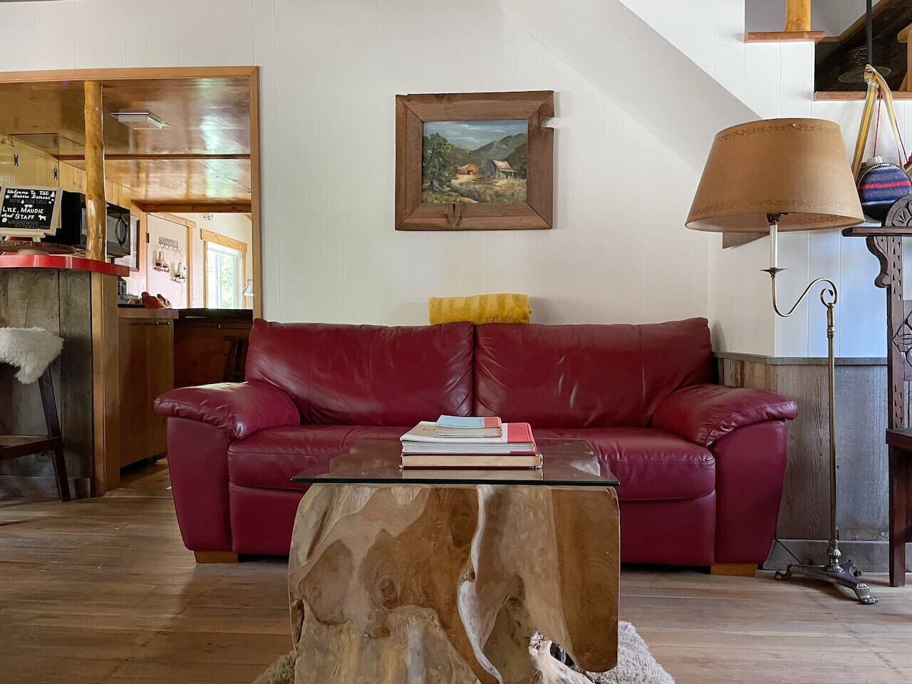 A living room with a red leather sofa, a coffee table with books, a wooden coffee table, a lamp, and a painting on the wall.