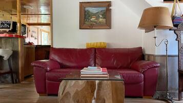 A living room with a red leather sofa, a coffee table with books, a wooden coffee table, a lamp, and a painting on the wall.