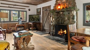 A cozy living room with a stone fireplace, wooden beams, a television, and a bookshelf. - Rustic Retreat|Pets OK, Near Village, Fireplace (Wrightwood)
