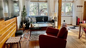 Een knus woongedeelte met een houten plafond, een bank, een rode fauteuil, een salontafel en een televisie.