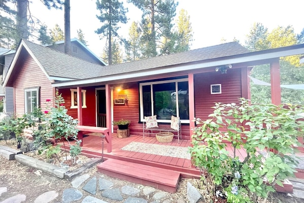 Welcome to this charming red cabin nestled among tall pines, featuring a cozy front porch perfect for relaxing mornings and peaceful evenings surrounded by nature.