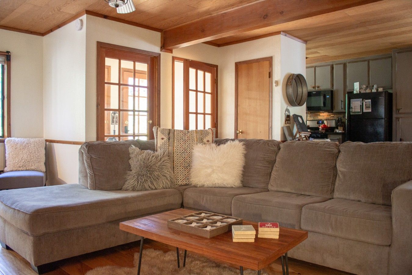 A cozy living room with a sectional sofa, a wooden coffee table, and a kitchen area in the background.